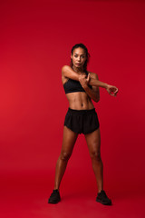 Strong young african sports fitness woman posing isolated over red wall background make exercises.