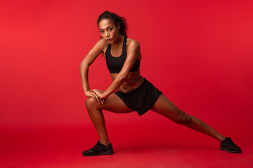 Fototapeta na wymiar Strong young african sports fitness woman posing isolated over red wall background make exercises.