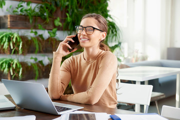 Attractive businesswoman making a call while sitting in front of laptop in the office and working