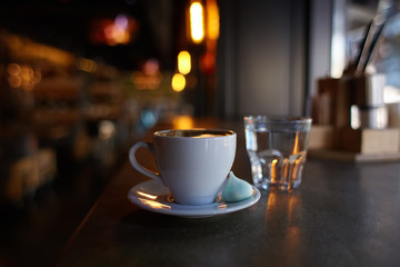 Cup of americano coffee in a white cup with a marshmallow on a saucer, shallow focus, dark background, bulb lights of caffeine
