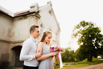 Young cute bride with bouquet of flowers hugging the groom on nature. Beautiful wedding couple outdoor portrait. Portrait of a loving couple. Wedding photo session. Second half. Newlywed