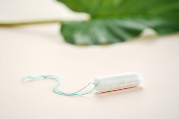 Hygienic tampon on a light background. In the frame of green floral leaf. Close-up. Light background.
