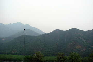 Panorama of high mountain ranges on the outskirts of a big city on the background of a misty sky.