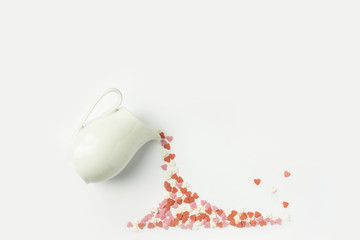 Multicolored sugar candy hearts imitating pouring liquid coffee tee from white milk jug. Creative flat lay. Valentine charity love donation generosity concept. Poster placeholder with copy space