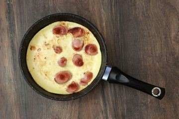 pan with scrambled eggs and sausages on an old tree