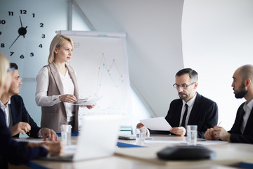 Young blonde businesswoman making report in front of audience at seminar or conference in boardroom