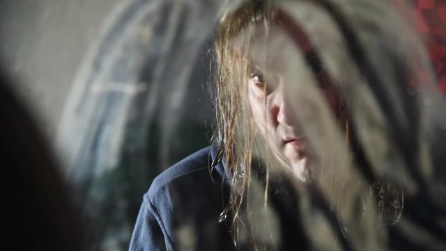 Depressed and angry man is sitting in front of his reflection in an old abandoned house