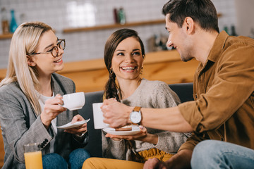 cheerful friends chatting while holding cups in cafe
