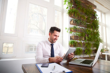 Businessman using digital tablet and computer while sitting at desk and working in the office