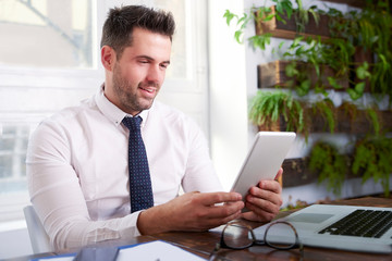 Businessman using digital tablet and computer while sitting at desk and working in the office