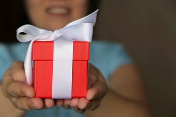 Smiling woman gives a red gift box. Female hands with gift close up, concept of Valentine's day or birthday