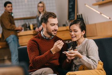 selective focus of handsome man feeding attractive woman with cake in cafe