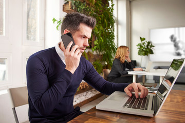 Businessman with making a call and working on laptop while sitting in the office