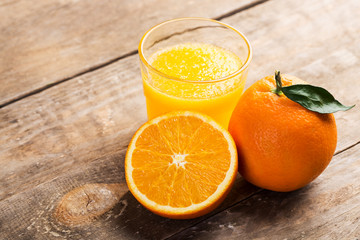Fresh orange juice and oranges on wooden table