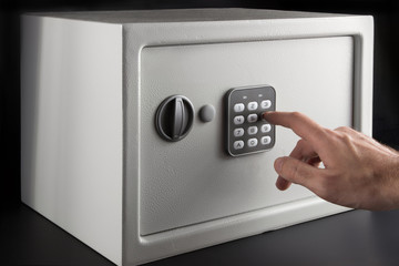 the hand opens a combination lock on the safe, a light safe on a dark background