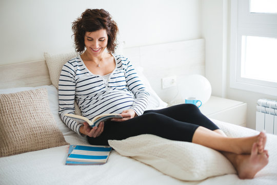 Happy pregnant woman reading on the bed