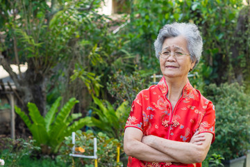 An senior woman wearing Cheongsam red shirt in the garden. Happy Chinese New Year.