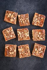 Shortbread cookies squares with caramel and nuts on black background.