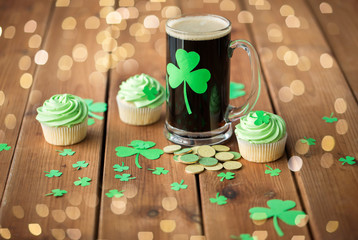 Fototapeta na wymiar st patricks day, holidays and celebration concept - glass of dark draft beer with shamrock, green cupcakes and gold coins on wooden table