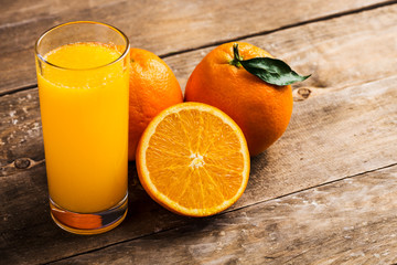 Glass of fresh orange juice with oranges on a vintage wooden background
