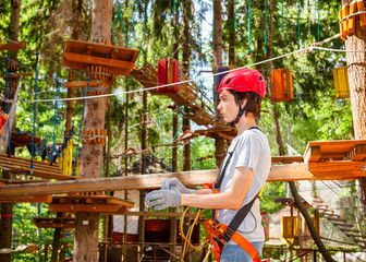 Teen boy wearing self belay safety equipment entering a ropes course in a treetop adventure park