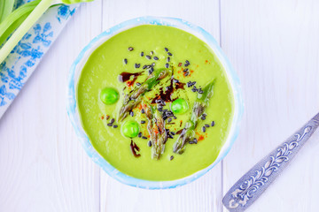 Homemade green cream soup with asparagus, green peas, black sesame seeds and pumpkin oil on a white background
