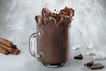 Cocoa splash in a transparent mug on a wooden table.