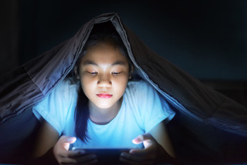 smiling girl lying in bed  playing a smartphone in social internet  in the dark light under the...