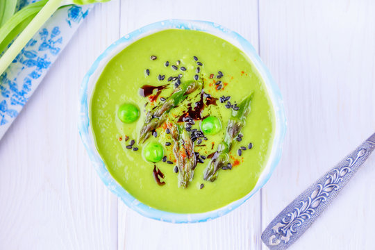 Homemade green cream soup with asparagus, green peas, black sesame seeds and pumpkin oil on a white background