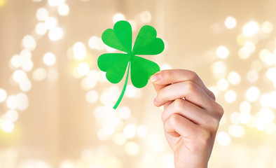fortune, luck and st patricks day concept - hand holding green paper shamrock over festive lights...
