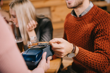 cropped view of female cashier holding terminal while man paying by credit card in cafe