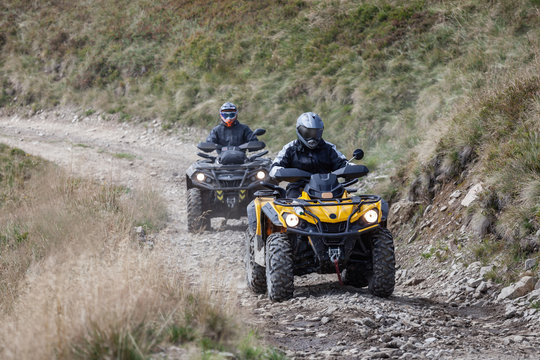 Front view of quad bikes zipping along a country road.