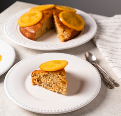homemade cake with slice of orange on top, white plates, grey backdrop
