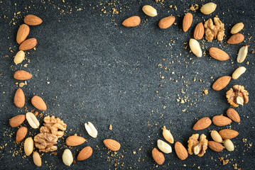 Fototapeta premium Nuts background of almonds, peanuts and walnuts with crumbs on black background.