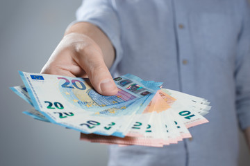 Hand giving euro banknotes on gray background