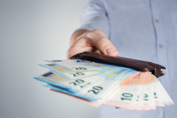 Hand giving a leather purse full of euro banknotes on gray background