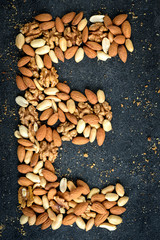 Nuts background of almonds, peanuts and walnuts with crumbs on black background.