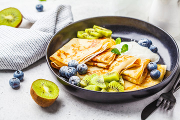Thin crepes with curd cream, kiwi and blueberries in a black plate.