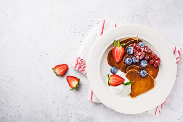 Pancakes in the shape of heart with berries, fruits and curd cream in a white plate, top view. Valentine's day concept.