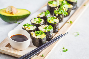 Vegan green sushi rolls with avocado, sprouts, cucumber and nori on wooden board, gray background.