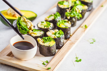 Vegan green sushi rolls with avocado, sprouts, cucumber and nori on wooden board, gray background. - obrazy, fototapety, plakaty
