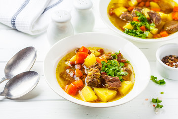 Traditional eintopf soup with meat, beans and vegetables in a white plate, white background.