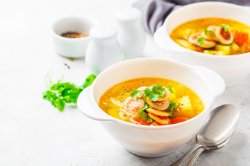 German potato soup with sausages and vegetables in white bowls, white background.