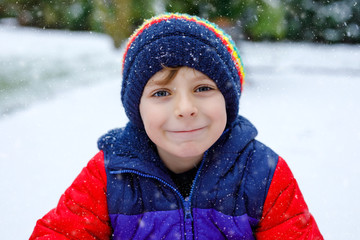 Portrait of little school kid boy in colorful clothes playing outdoors during snowfall. Active...
