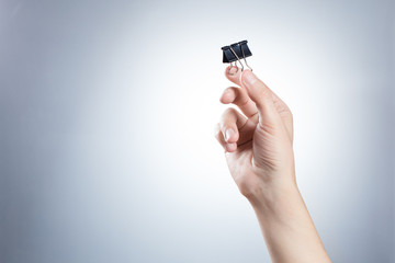 Hand holding a binder clip on gray background
