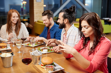 technology, lifestyle and people concept - bored woman dining with friends and messaging on smartphone at restaurant