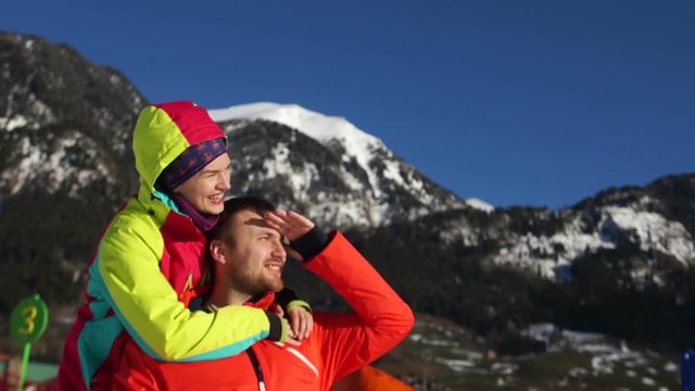 Lovely couple is resting in the mountains in winter. A man and a woman in red ski jackets on the background of snowy mountain slopes