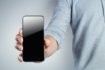 Hand showing black smartphone on gray background