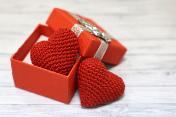 Valentine gift box with red knitted hearts on light wooden table. Romantic present in Valentine's day, wedding concept