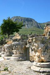 The tops of corinthian columns sit among the ruins at Corinth, Greece.